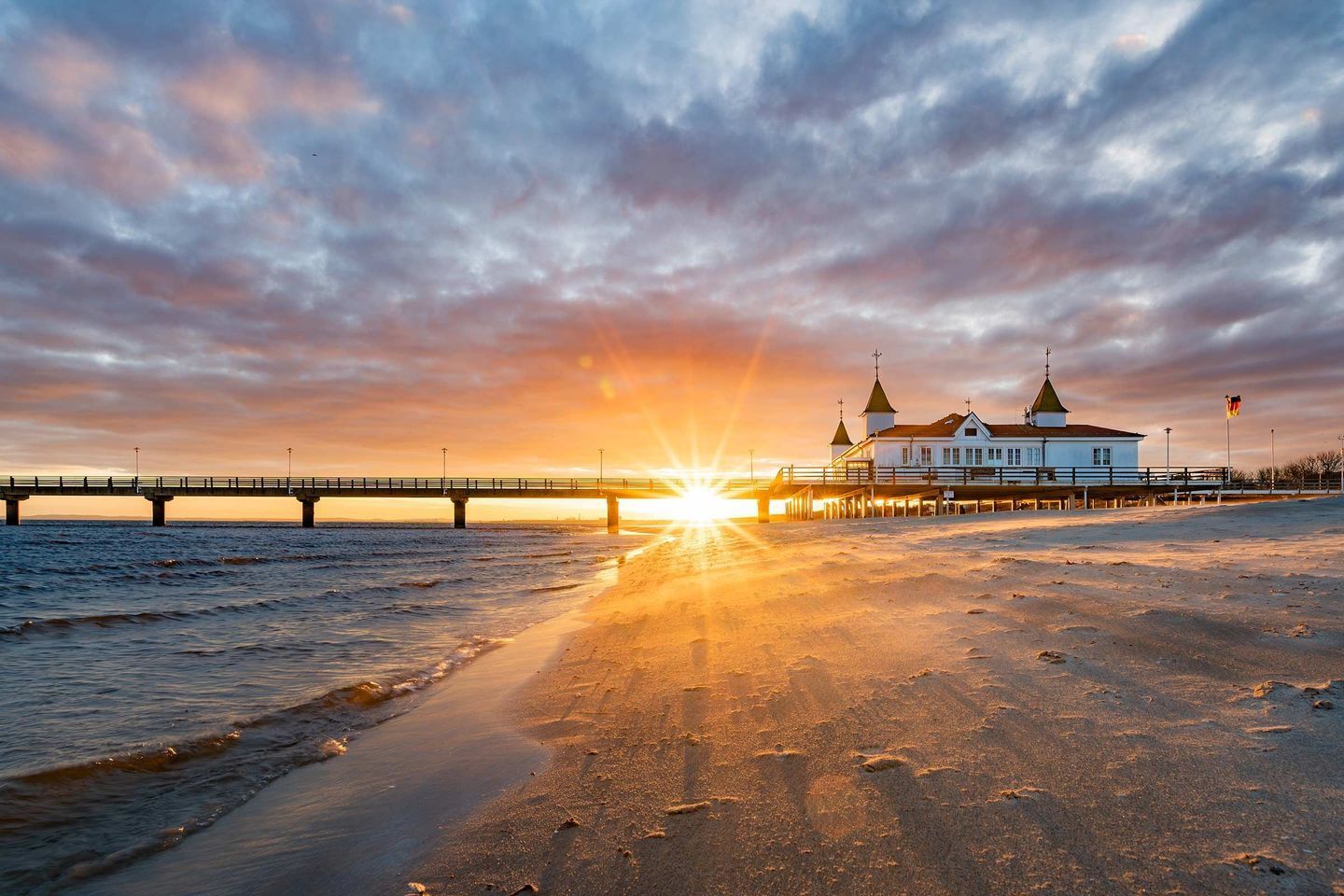 A beach with a pier and a building with two towers.