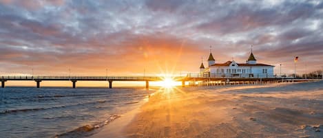 A beach with a pier and a building with two towers.