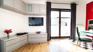 A modern living room with a flat-screen TV, a dining area with a checkered floor, and a red accent wall.