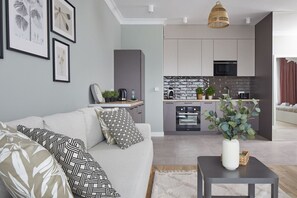 Una sala de estar moderna con un sofá gris, una mesa de centro y una cocina al fondo con armarios grises y un salpicadero negro.
