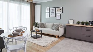 Una sala moderna con un sofá, una mesa de comedor y sillas. Hay una cafetera en el mostrador y un reloj en la pared.