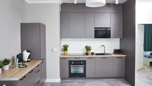 Eine moderne Küche mit grauen Schränken, einer Holz Arbeitsplatte, einem eingebauten Ofen und einer Mikrowelle. Auf der Arbeitsplatte befinden sich zwei Blumentöpfe.