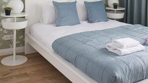 Ein ordentlich bezogenes Bett mit blauer Bettdecke und Kissen, ein weißer Kopfteil und eine Wand mit floralem Wandpapier.