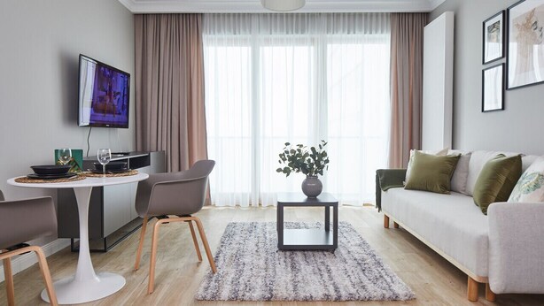 Ein modernes Wohnzimmer mit Sofa, Couchtisch, Fernseher und Essbereich mit Stühlen und Tisch.