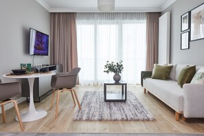 A modern living room with a sofa, a coffee table, a TV, and a dining area with chairs and a table. - Metro Imielin 9th Floor Apartment (Warszawa)