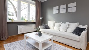 Ein modernes Wohnzimmer mit einem weißen Sofa, einem weißen Couchtisch und einem Fenster mit Vorhängen.