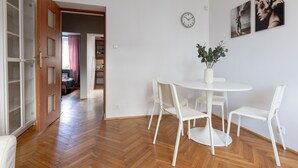 Ein Zimmer mit Holzboden im Fischgrätmuster, weißen Möbeln, einer Uhr und zwei gerahmten Bildern an der Wand.