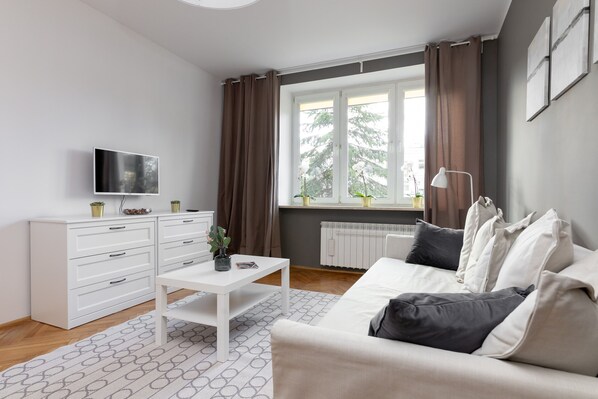 A modern living room with a white sofa, a coffee table, a TV, and a window with curtains.
