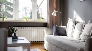 Un salon moderne avec un canapé blanc, une petite table sur laquelle est posé un vase de fleurs et une fenêtre agrémentée de deux plantes en pot.