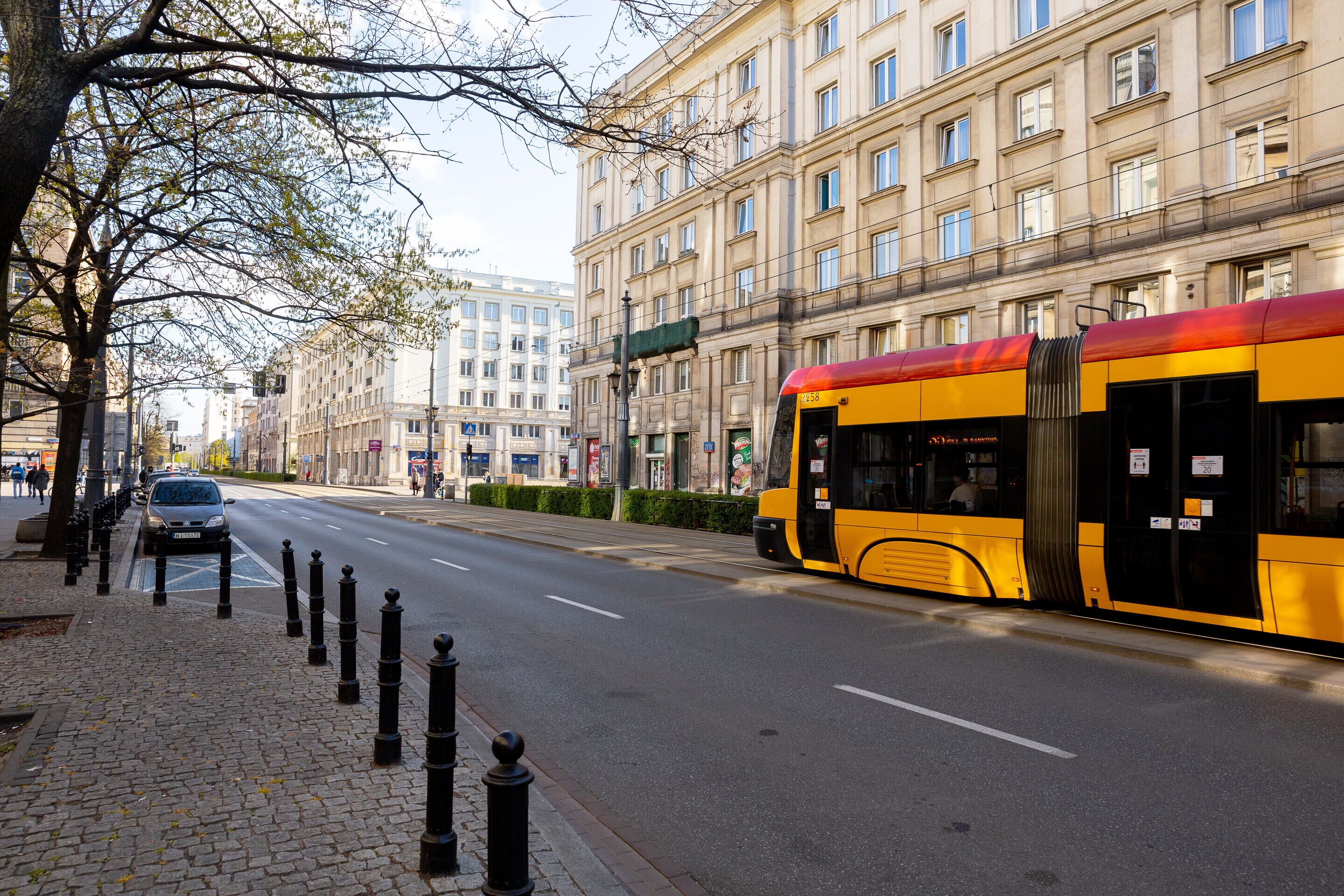 A city street with a yellow tram, buildings, and a sidewalk.