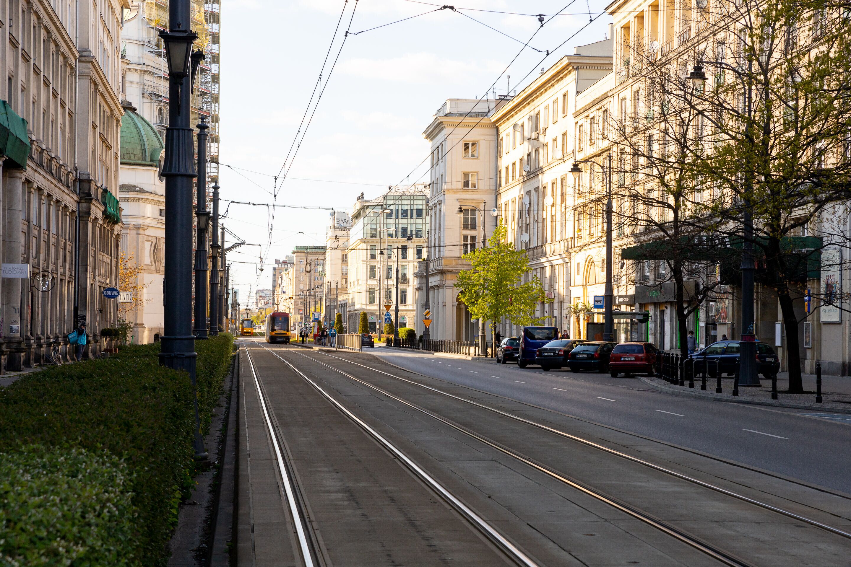A street with tram tracks, buildings, and parked cars.