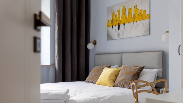 Een moderne hotelkamer met een opgemaakt bed, een stadsgezichtschilderij aan de muur, en een bureau met een stoel.