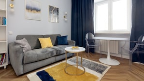 Een moderne woonkamer met een grijze bank, een klein rond tafeltje en een boekenkast.