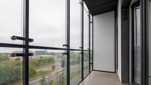 Moderni parveke, jossa on suuret lasiovet ja -ikkunat, ja josta avautuu näkymä kaupunkimaisemaan ja kadulle.