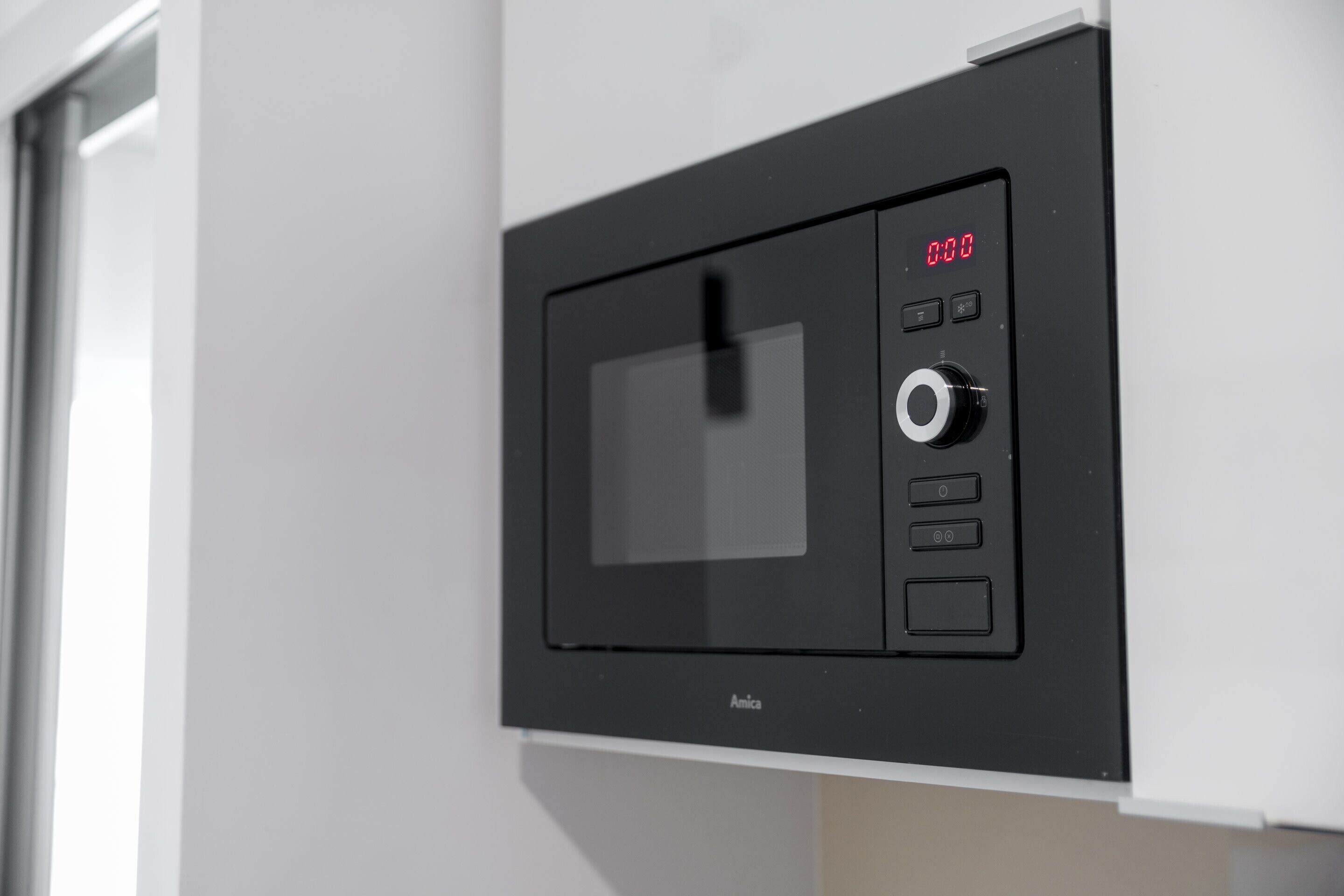 A black microwave oven with a digital display and control buttons mounted on a white wall.