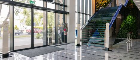 A modern building entrance with a glass door, a staircase with blue LED lights, and a green plant wall.