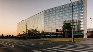Un edificio moderno con fachada de vidrio, un paso de cebra en la parte delantera y una farola cerca.
