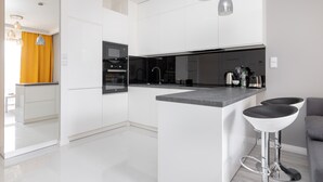 A modern kitchen with white cabinetry, a central island with bar stools, and stainless steel appliances. - Wilanów Gardens with Balcony (Warszawa)