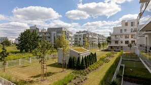 A residential area with modern apartment buildings, a grassy courtyard, and a small green-roofed structure. - Wilanów Gardens with Balcony (Warszawa)