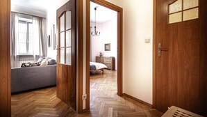 A room with a herringbone wooden floor, a grey sofa, a wooden door with a window, and a bed with a wooden headboard. - Świętojsańska  Old Town  Apartment (Warszawa)