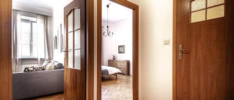 A room with a herringbone wooden floor, a grey sofa, a wooden door with a window, and a bed with a wooden headboard.