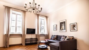 A living room with a sofa, a coffee table, a TV, and a chandelier. - Świętojsańska  Old Town  Apartment (Warszawa)