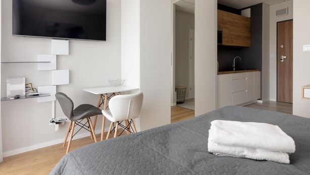 Una habitación de hotel moderna con una cama grande, un televisor de pantalla plana, un escritorio con una silla y una kitchenette.