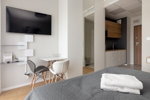 Une chambre d’hôtel moderne dotée d’un grand lit, d’une télévision à écran plat, d’un bureau avec une chaise et d’une kitchenette.