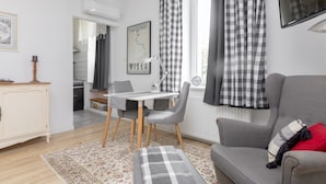 A modern living room with a grey sofa, a dining table with chairs, a checkered rug, and a kitchen in the background.