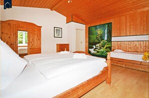 Quarto estilo cabana de madeira com uma cama grande, cabeceira de madeira, um quadro na parede e uma pintura de uma paisagem florestal.