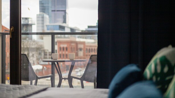 A balcony with a table and chairs, overlooking a cityscape with buildings. - Warsaw Spire Stylish Apartment (Warszawa)