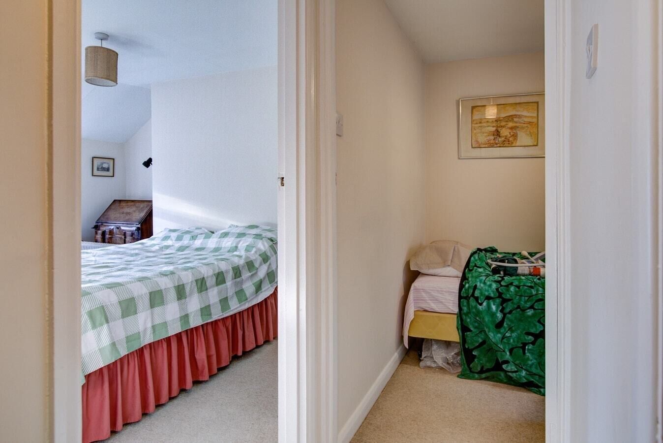 A narrow hallway leading to a bedroom with a bed, a small table, and a chair.