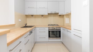 Een moderne keuken met witte kastjes, een houten aanrecht, een ingebouwde oven en een gasfornuis.