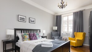 Een keurig opgemaakt slaapkamer met een bed, nachtkastjes, een stoel en een raam met gordijnen.
