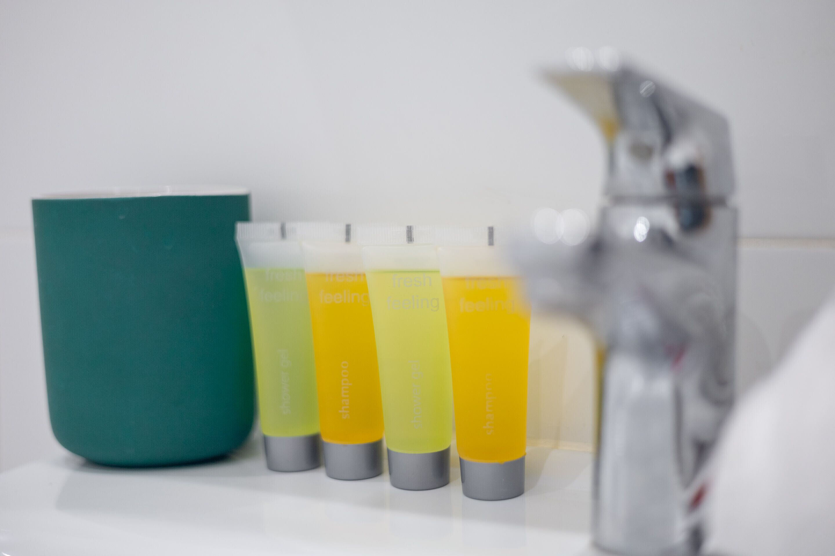 Et badeværelse med en hvid vask, en grøn sæbedispenser og fire shampoo flasker.