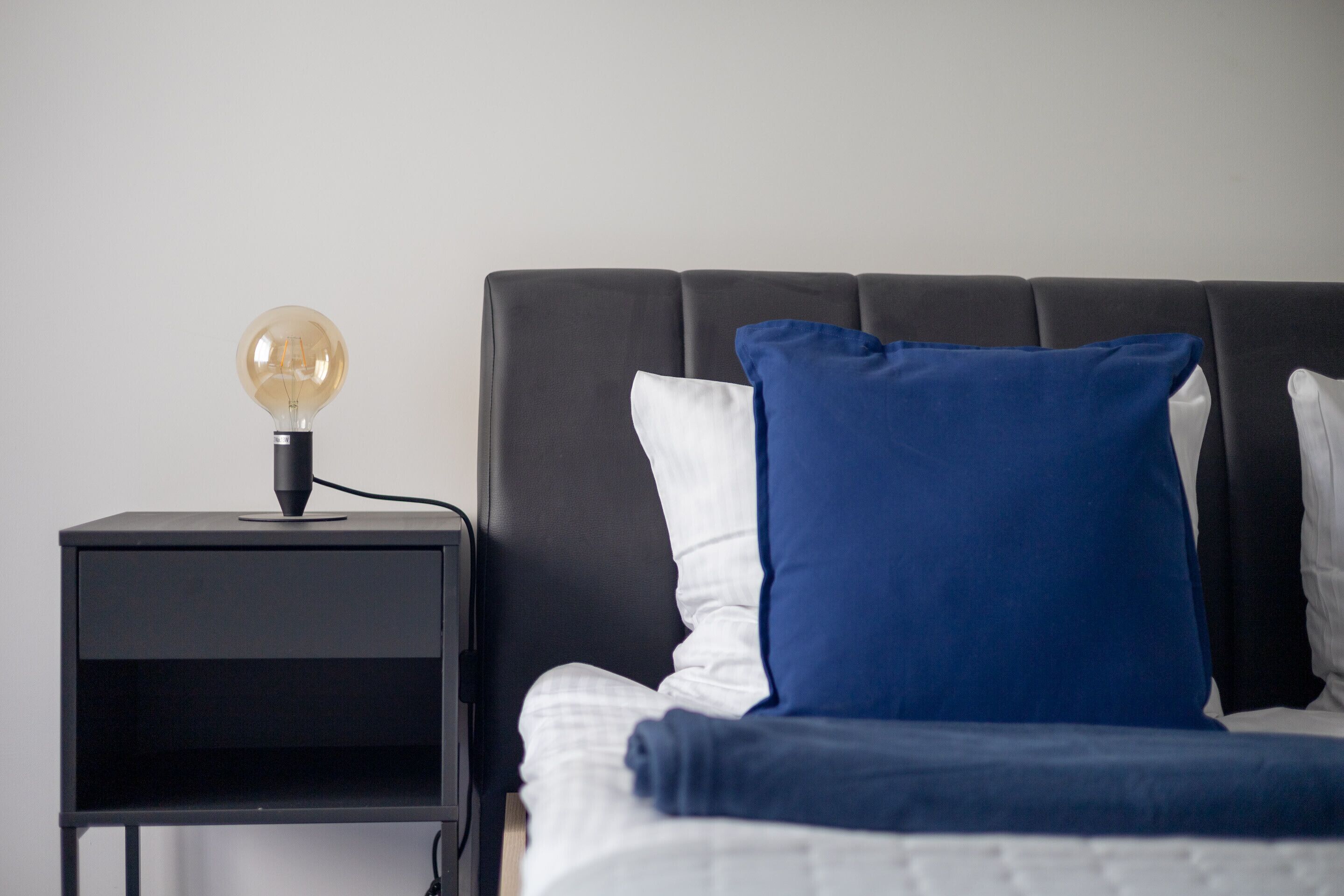 A bed with a black headboard, white and blue pillows, and a bedside table with a lamp.