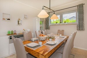 Un coin repas avec une table en bois dressée pour quatre personnes, entourée de chaises, et une cuisine en arrière-plan.