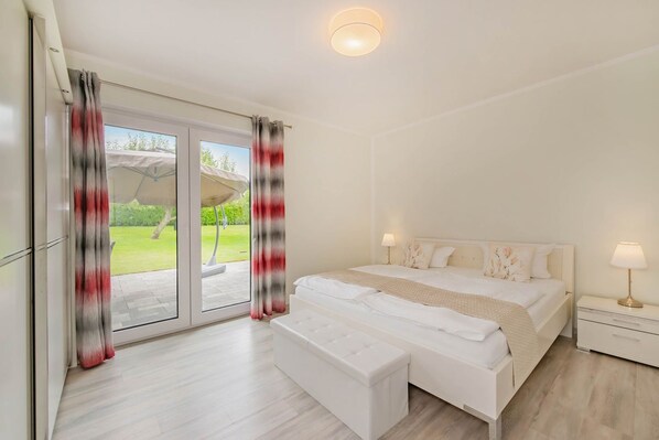 Une chambre à coucher comprenant un lit, des tables de chevet, un banc et une porte-fenêtre coulissante donnant sur un espace extérieur.