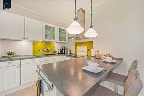 A modern kitchen with white cabinets, a central island with seating, and pendant lighting.