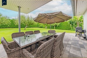 An outdoor patio with a glass-top table, wicker chairs, and a large umbrella. - Ferienhaus Zirchow 4 - Modernes, 125 m² Ferienhaus für bis zu 8 Gäste, Garten, Grillmöglichkeiten, (Zirchow)