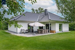 A modern house with a tiled roof, a covered patio with outdoor furniture, and a barbecue setup. - Ferienhaus Zirchow 4 - Modernes, 125 m² Ferienhaus für bis zu 8 Gäste, Garten, Grillmöglichkeiten, (Zirchow)