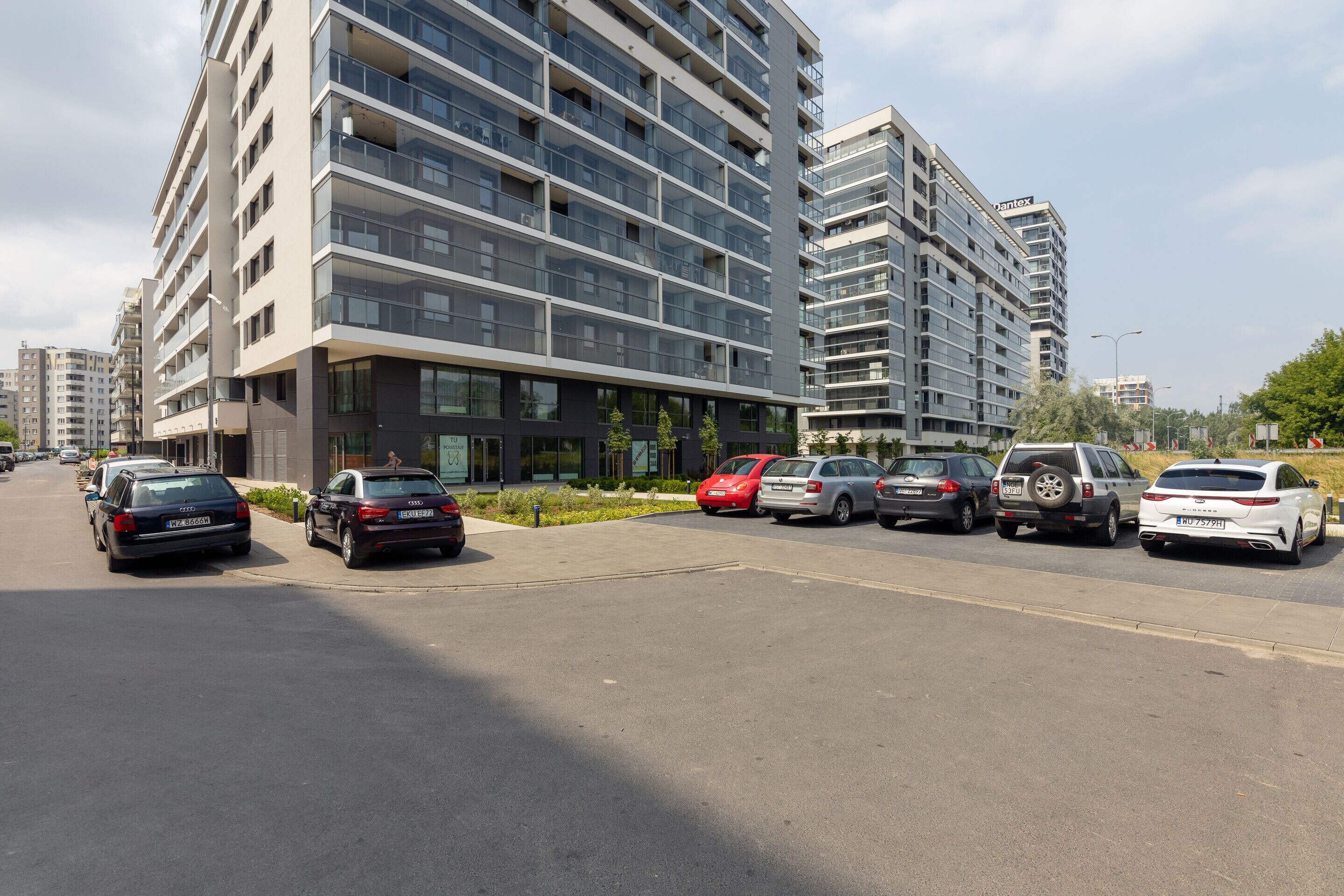A modern multi-story residential building with a parking lot in front.