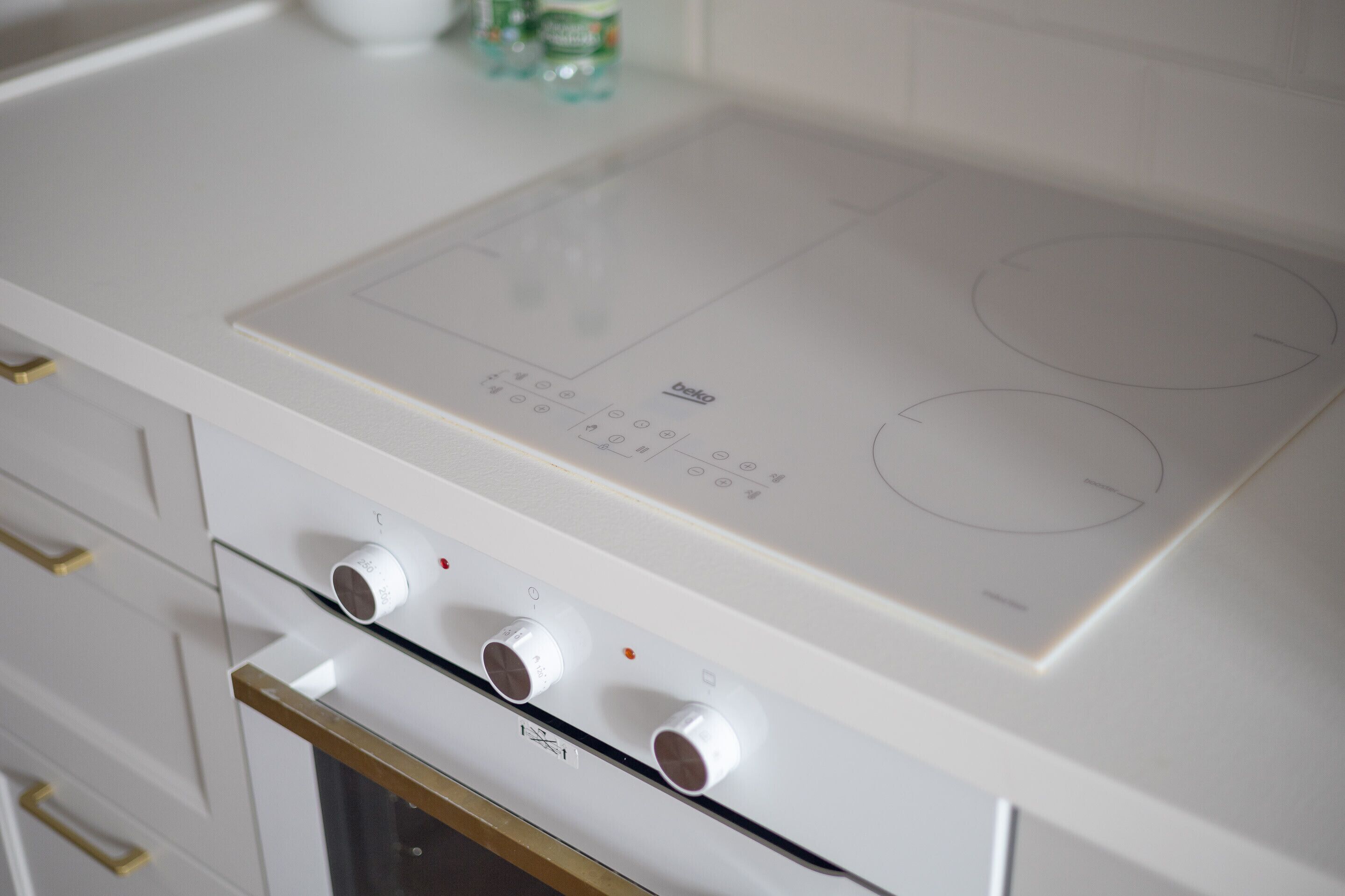 Una cocina moderna con placa vitrocerámica integrada, horno de acero inoxidable y encimera blanca.