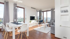 Una sala de estar moderna con comedor, ventanas grandes, televisor de pantalla plana y vista a la ciudad.