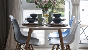 A dining area with a table set for two, featuring a vase of flowers, a pitcher, and various bowls and cups.