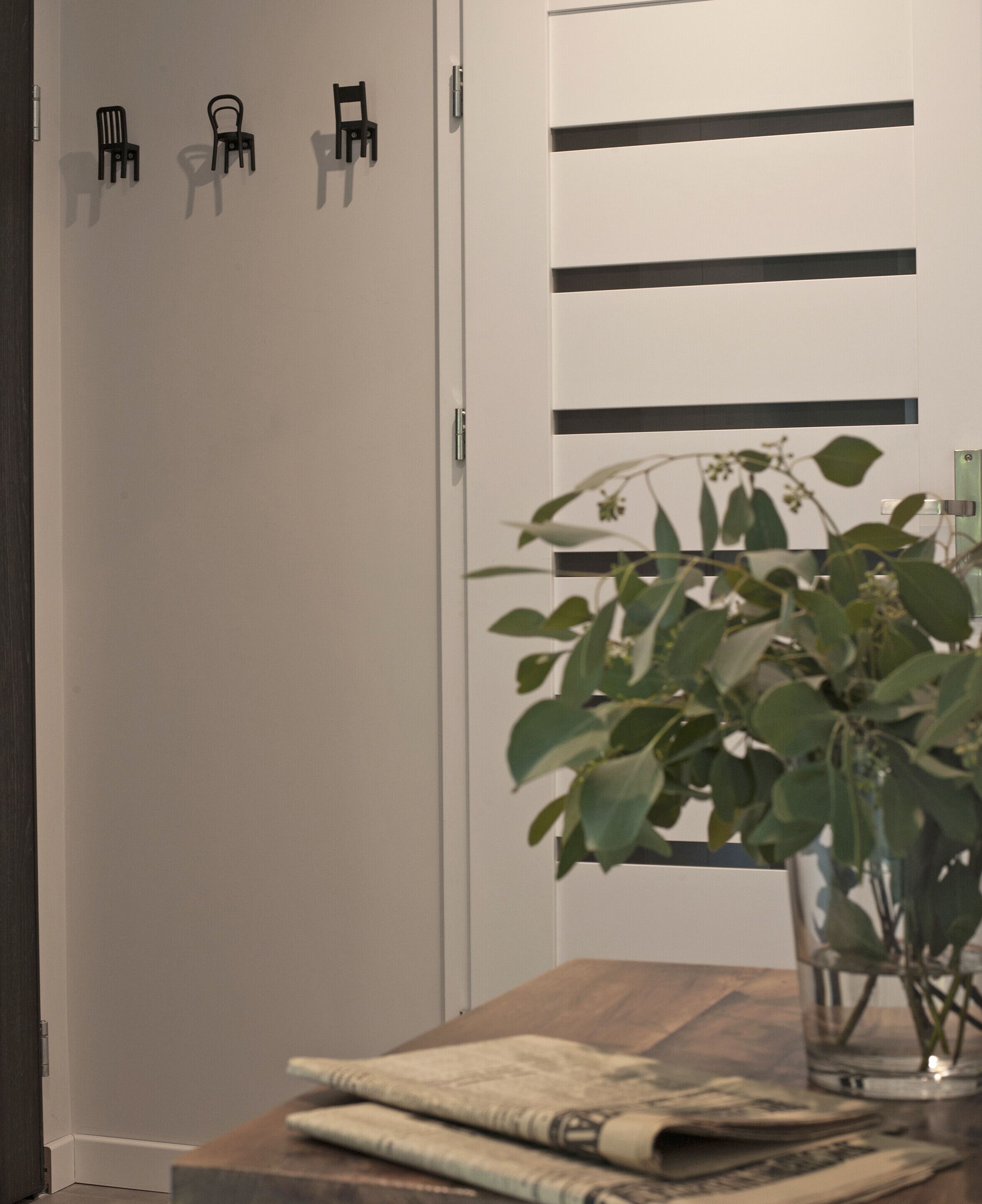 Une pièce avec une table en bois, une plante en pot et une armoire blanche ornée de lignes horizontales noires.