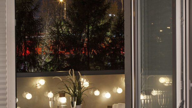 A balcony with a table set for two, a potted plant, and string lights.