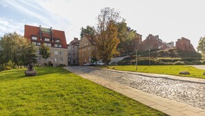 A paved walkway leading to a building with a red roof, surrounded by greenery and a stone pathway.