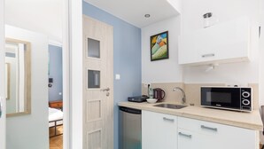 A compact kitchen with a microwave, sink, and dishwasher. A door leads to a bedroom with a bed.