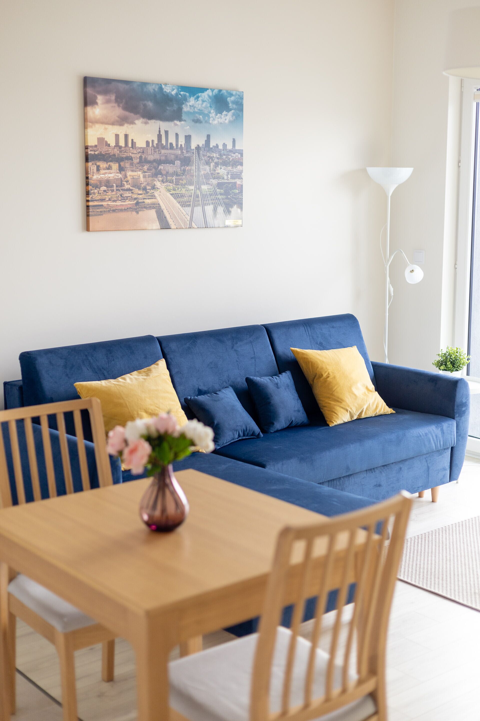 Una sala moderna con un sofá azul, una mesa de comedor de madera y un cuadro de un paisaje urbano en la pared.